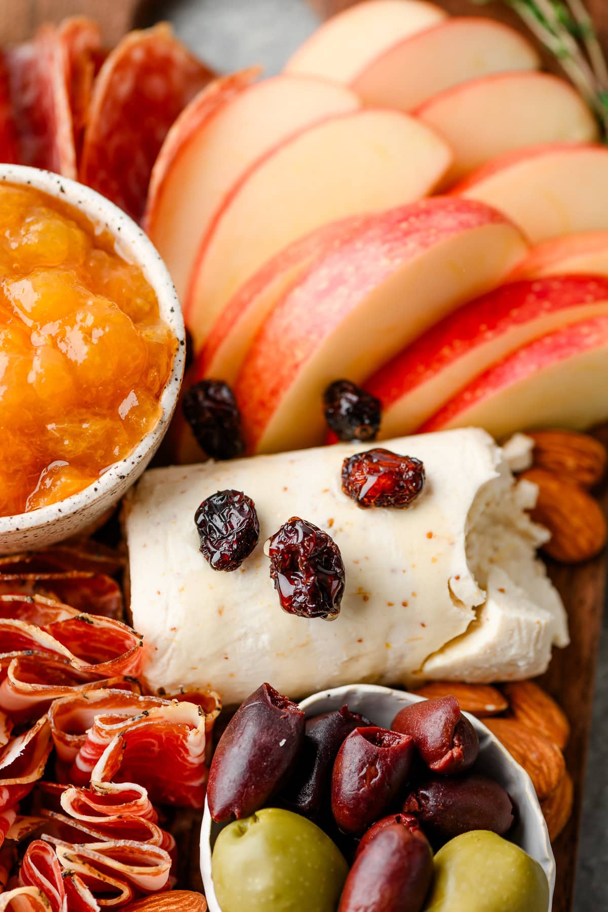 Closeup of goat cheese topped with honey and dried cranberries on a charcuterie board