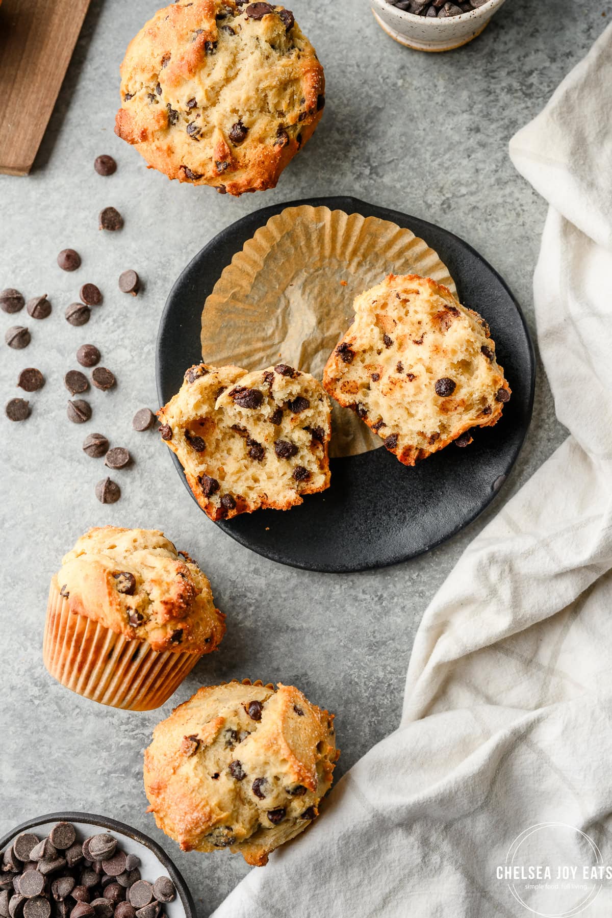 A gluten free chocolate chip muffin torn open on a small plate, surrounded by chocolate chips and more muffins