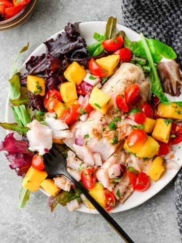 Overhead view of grilled walleye over spring greens and smothered in mango salsa
