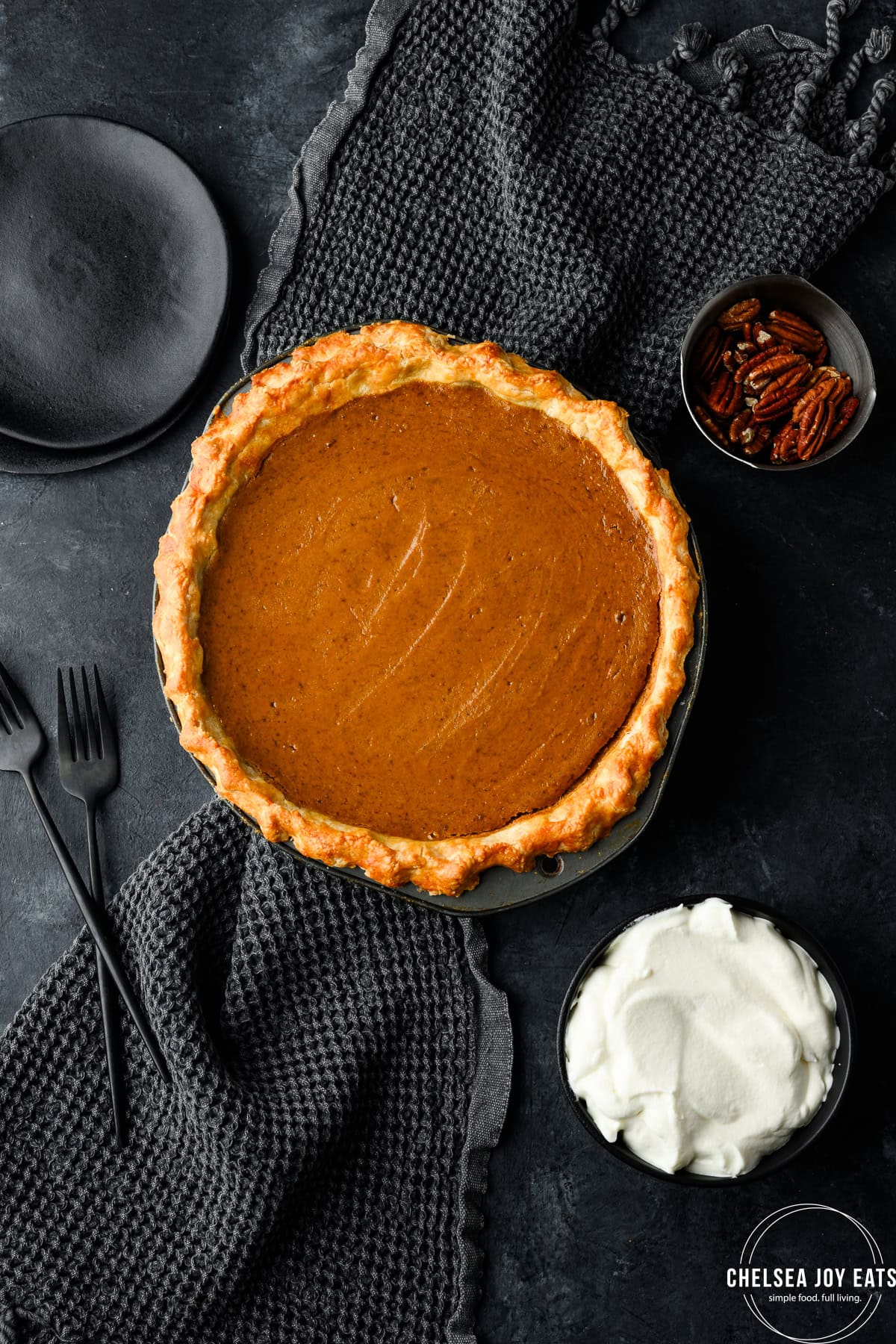 Whole gluten free pumpkin pie surrounded by plates and a bowl of fresh whipped cream