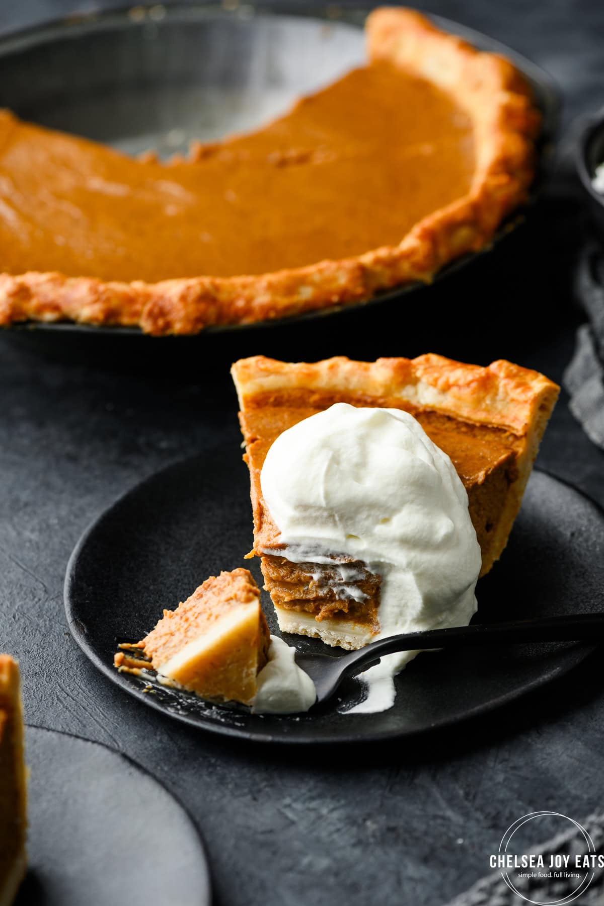 Closeup of a pumpkin pie with a piece removed by a fork, topped with whipped cream