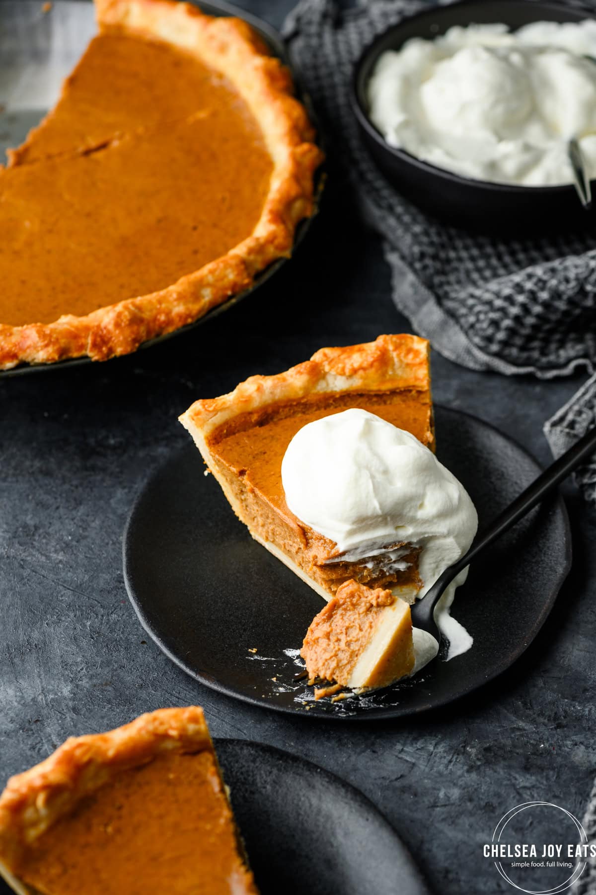 Pumpkin pie with a dollop of whipped cream, with a piece taken out by a fork