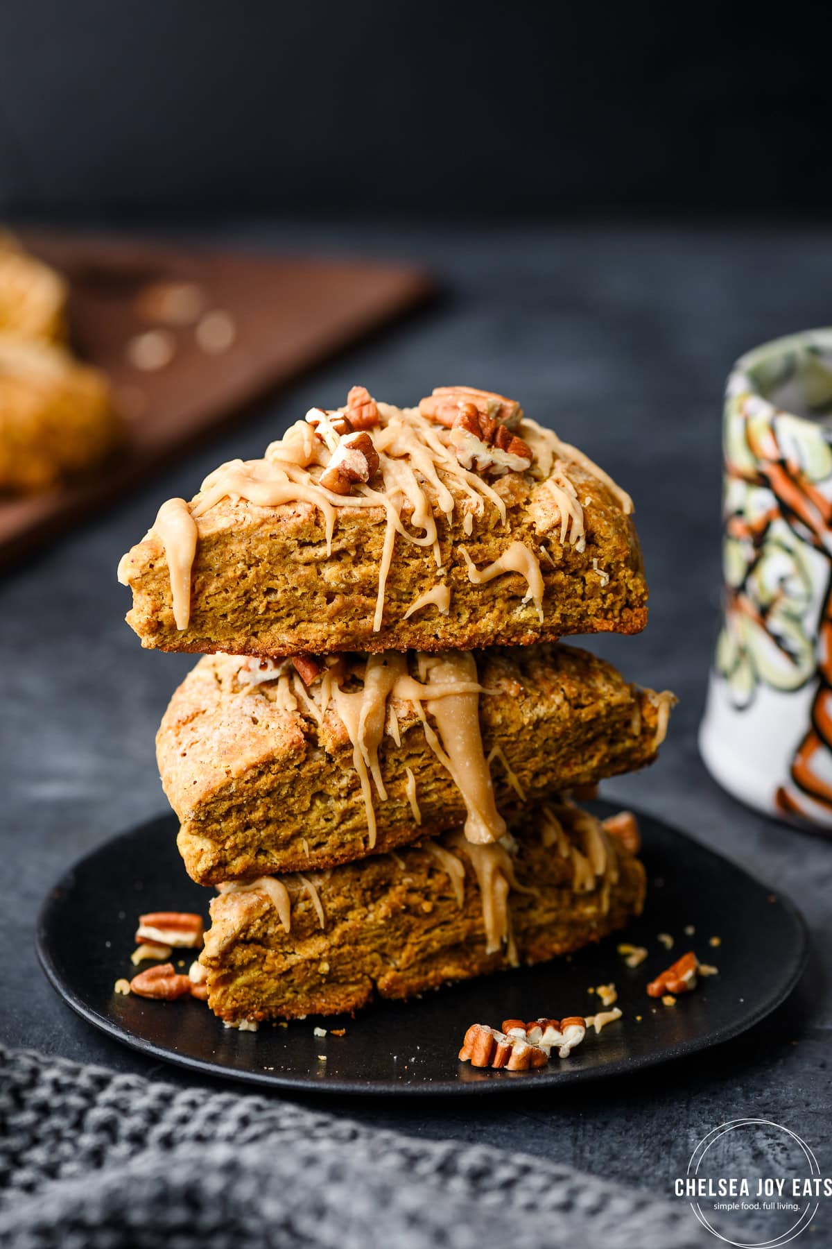 Stack of pumpkin scones on a plate with a mug of coffee in the background