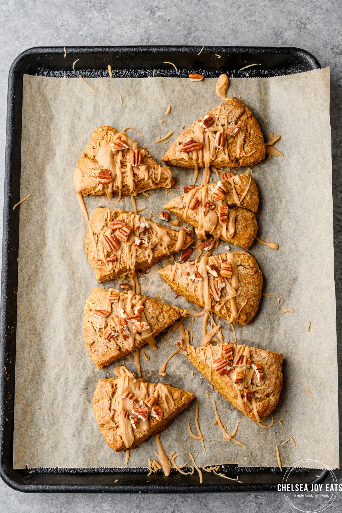 Gluten Free Pumpkin Scones arranged on a baking sheet, drizzled in maple icing and topped with pecans