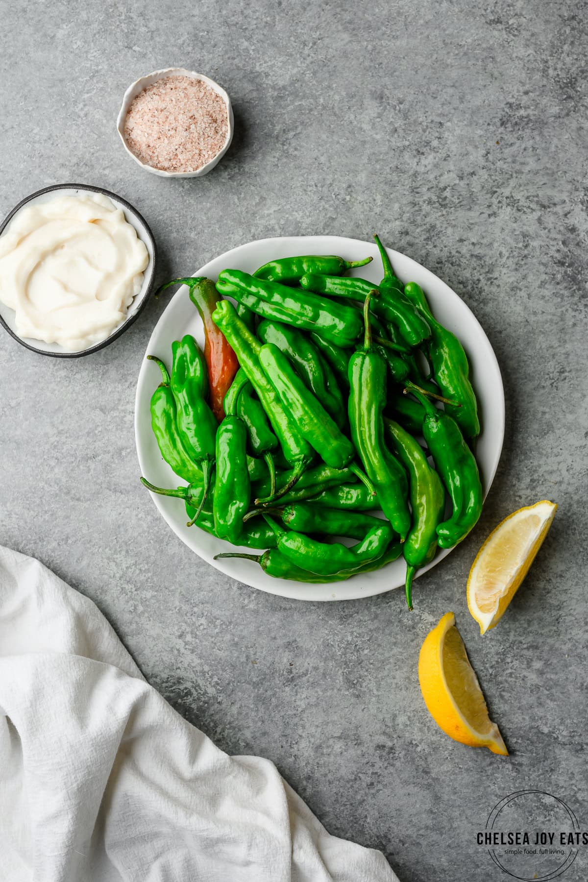 Plate of raw shishito peppers with lemon wedges and a small dish of aioli