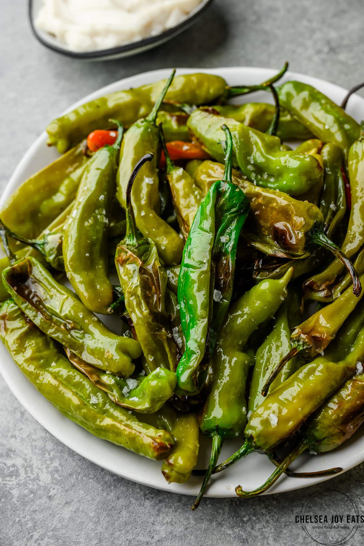 Closeup of blistered oven roasted shishito peppers garnished with flaky sea salt