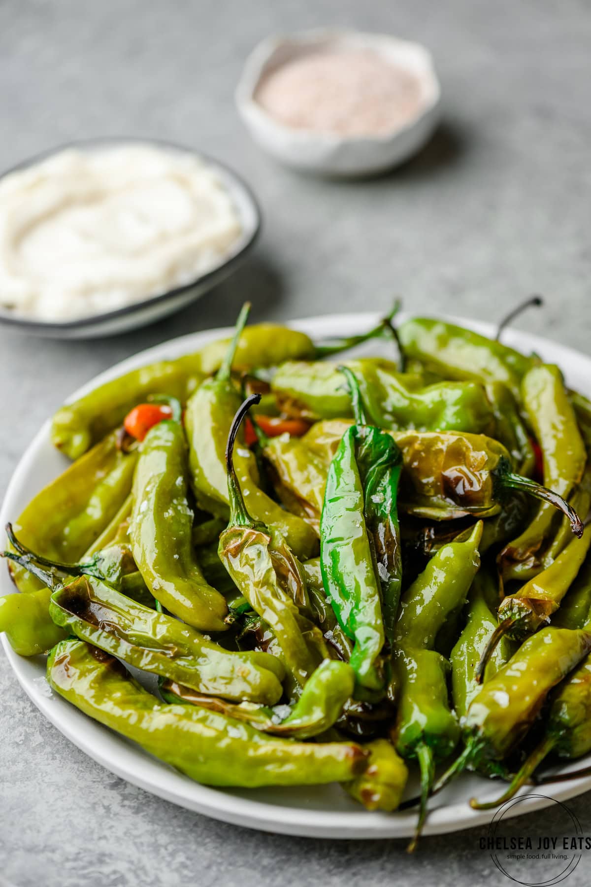Plate piled high with roasted shishito peppers on a light background