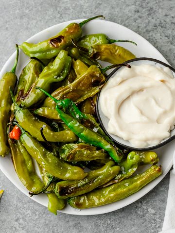 Plate of oven roasted shishito peppers with a dish of garlic aioli for dipping