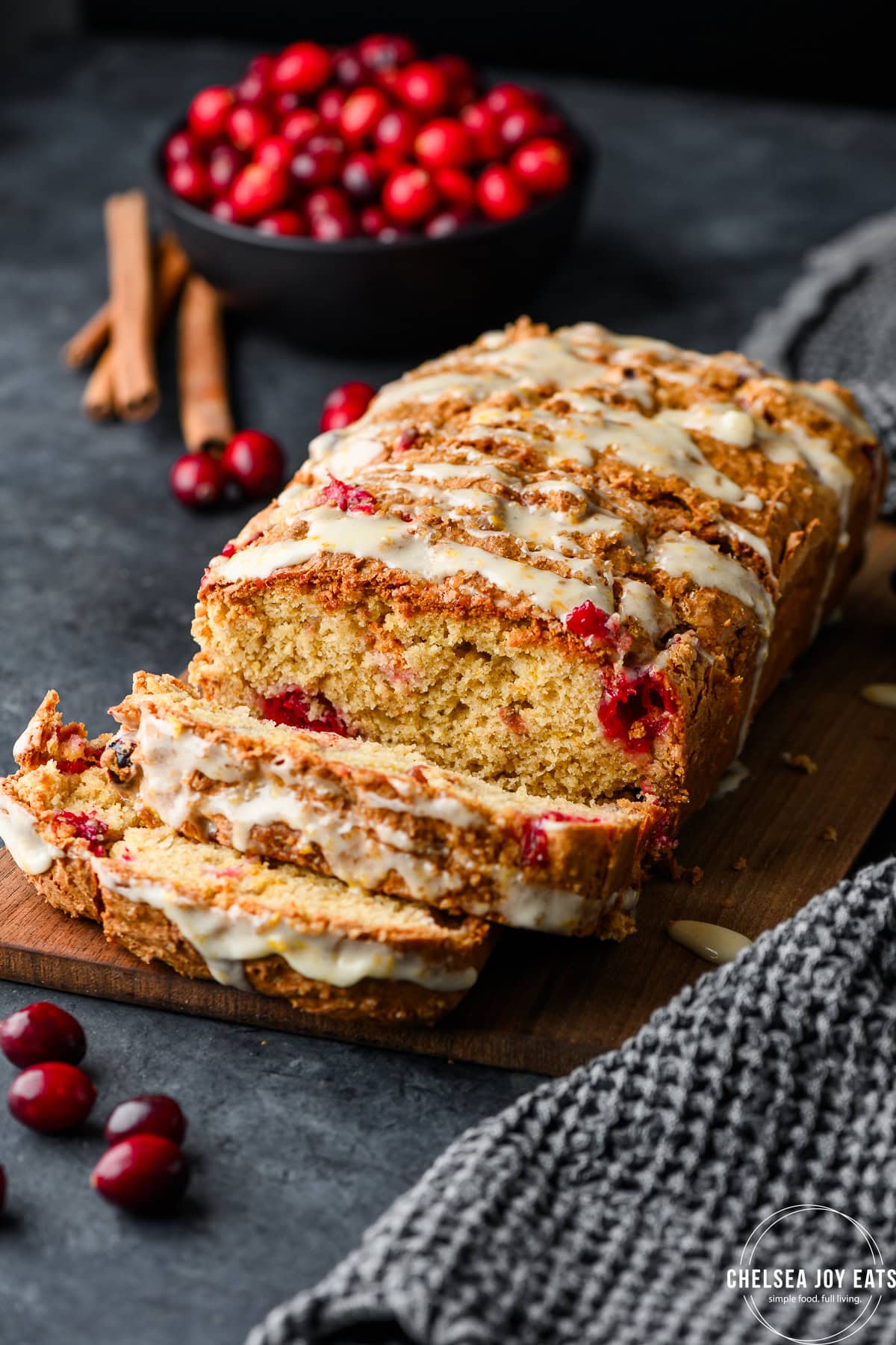 Loaf of gluten free cranberry bread drizzled with orange icing, partially sliced on a dark background
