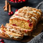 Loaf of gluten free cranberry bread, partially sliced on a dark background