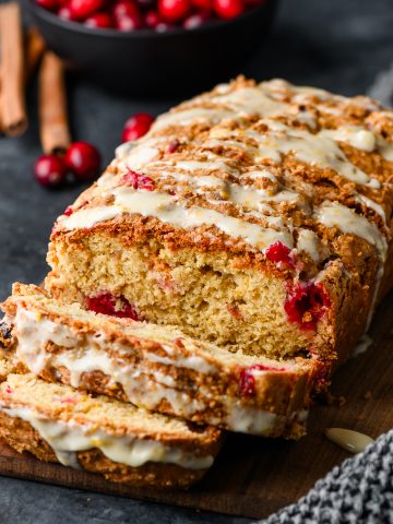 Loaf of gluten free cranberry bread, partially sliced on a dark background