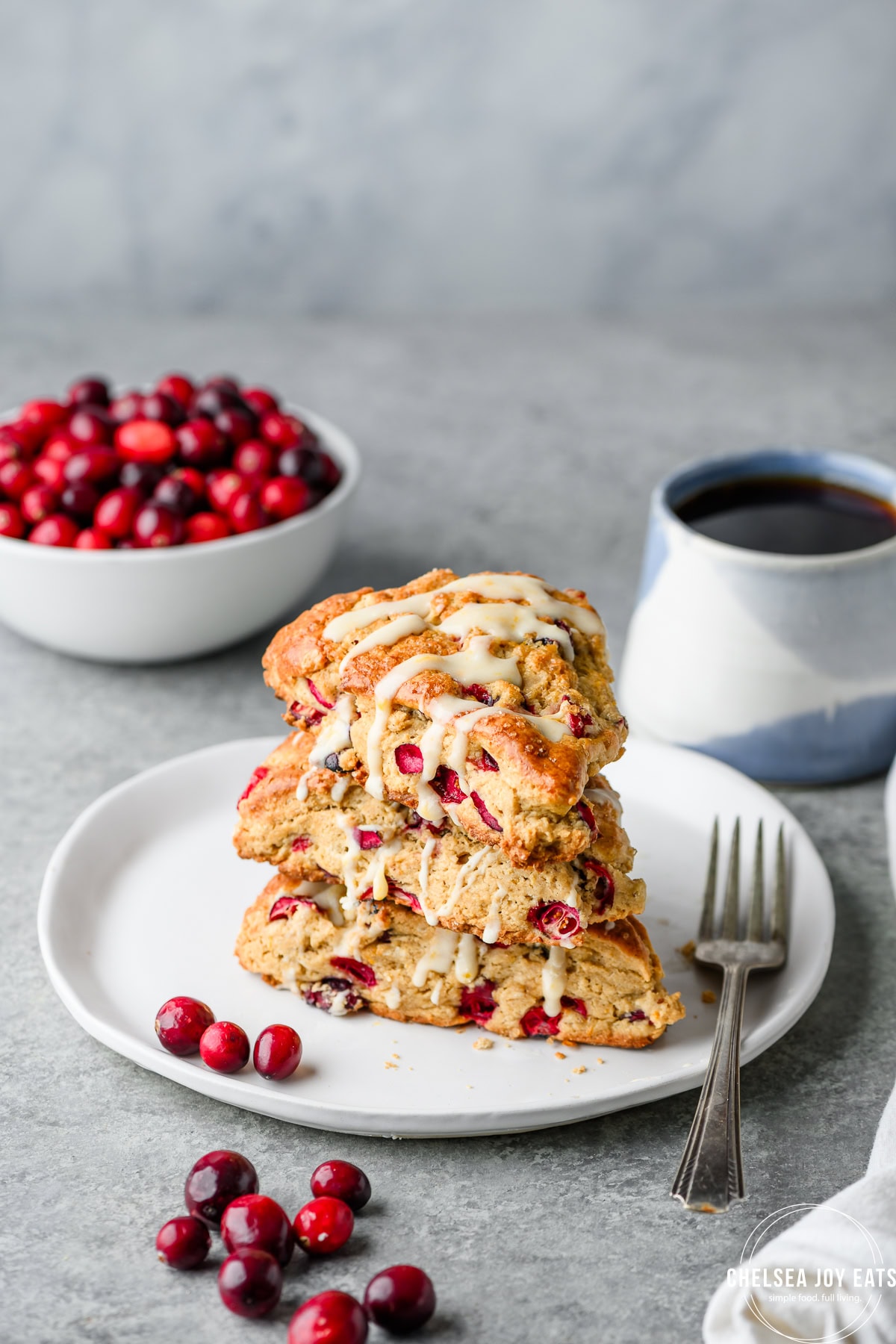 Gluten free cranberry orange scones drizzled in orange icing and stacked on a plate