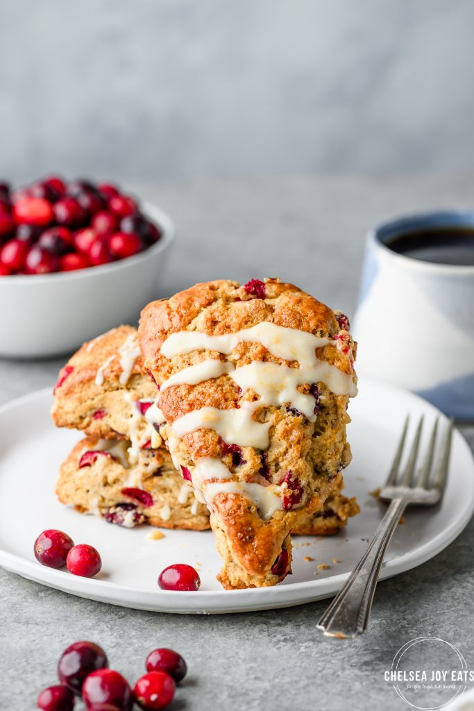 Gluten free cranberry orange scones on a plate with a cup of coffee and fresh cranberries in the background