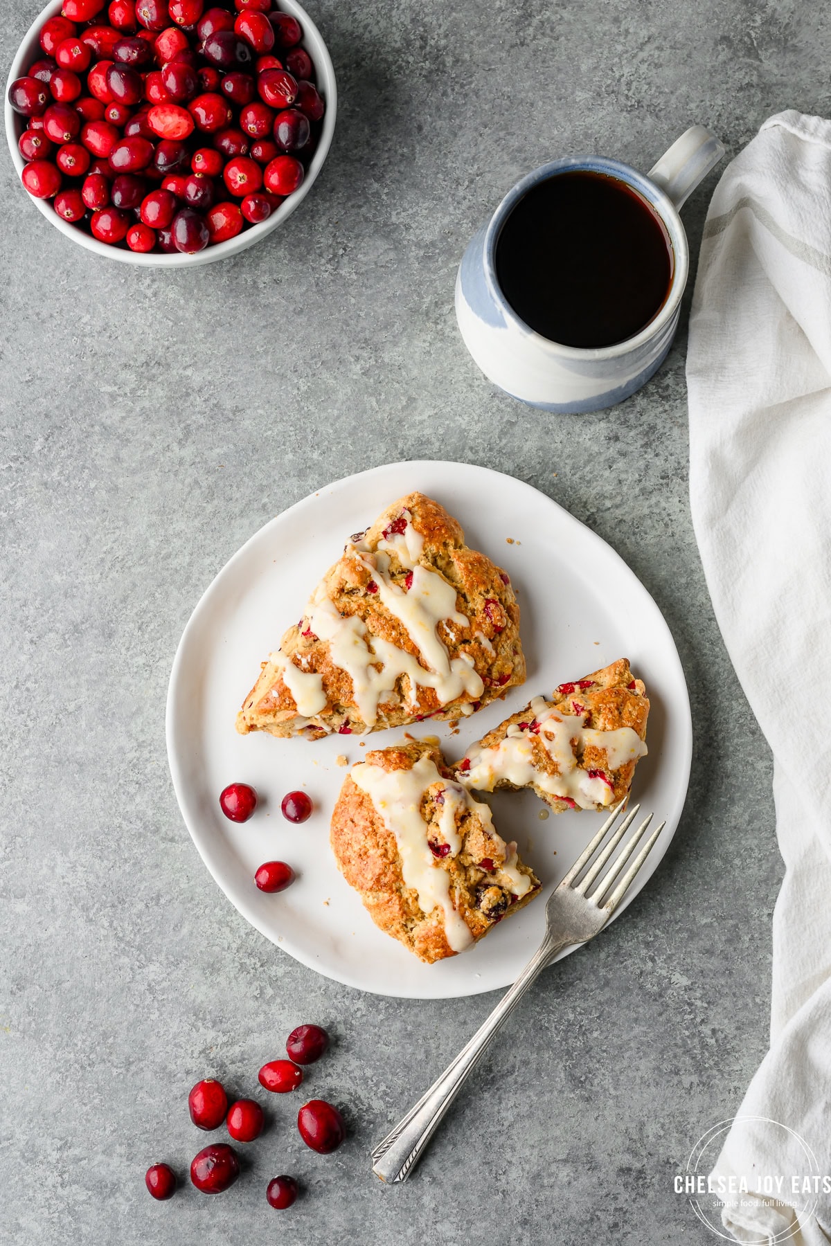 Overhead view of gluten free scones on a plate with a fork, with a cup of coffee and fresh cranberries in the frame
