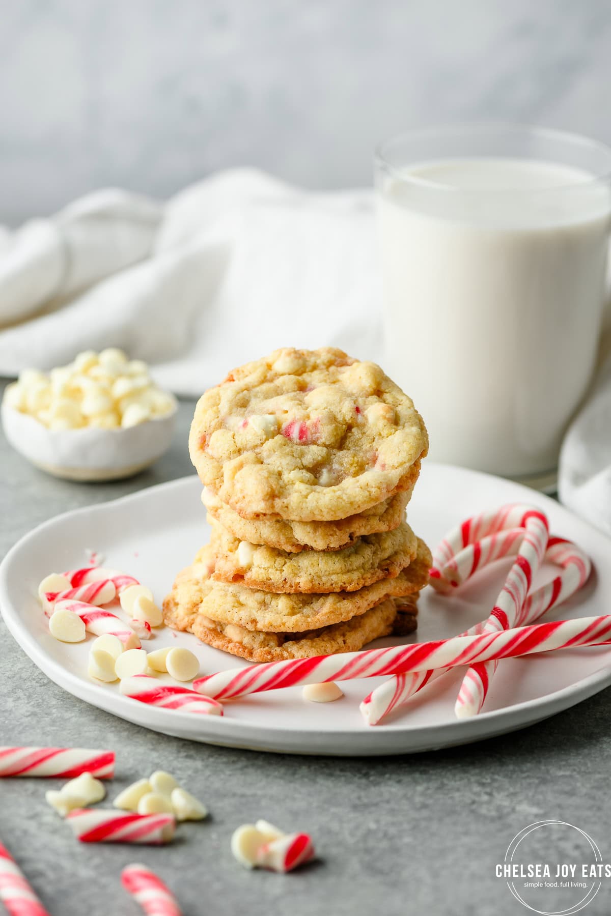 Stack of gluten free white chocolate peppermint cookies on a plate with candy canes and white chocolate chips as garnish