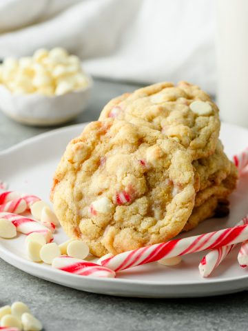 Gluten free white chocolate peppermint cookies piled on a plate, garnished with candy cane and white chocolate chips
