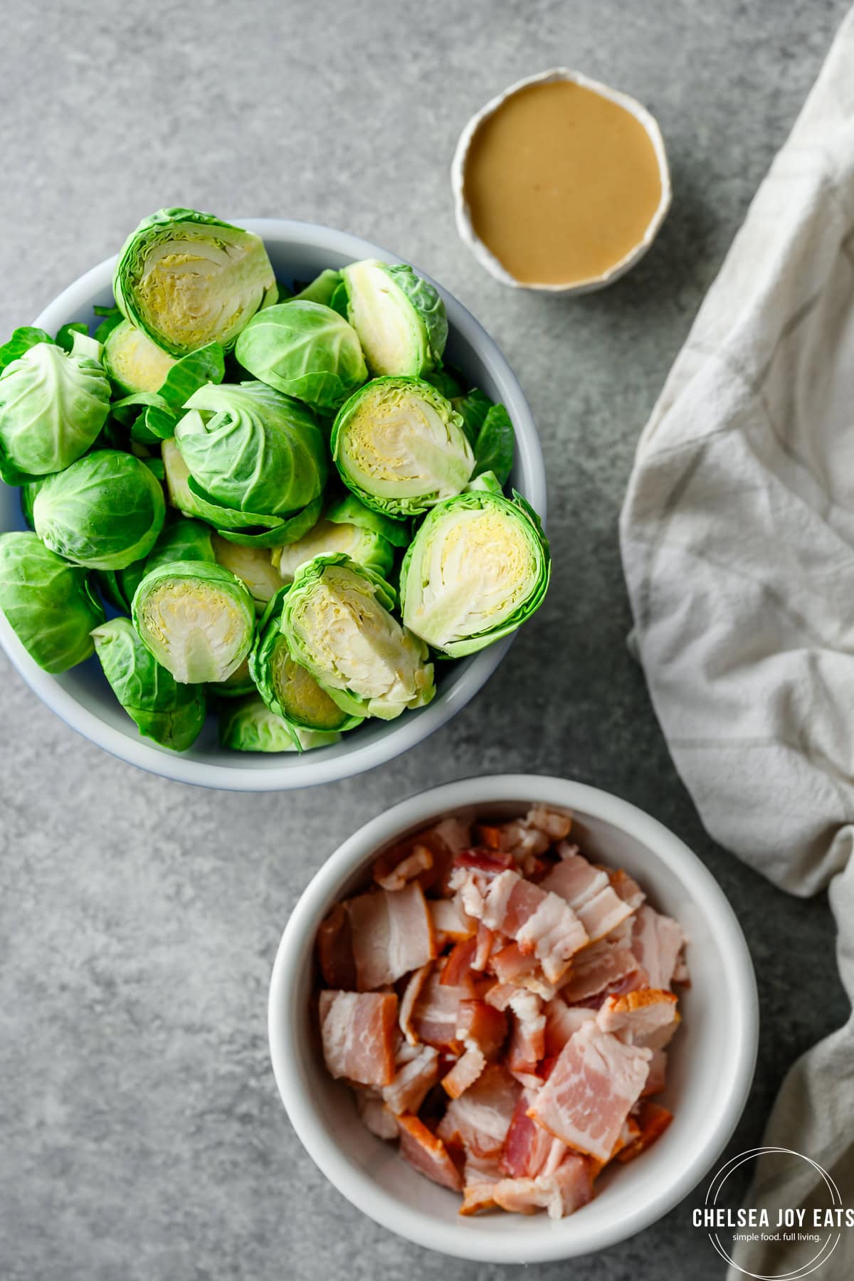 Overhead view of bowls with raw brussels sprouts, uncooked bacon, and honey mustard sauce