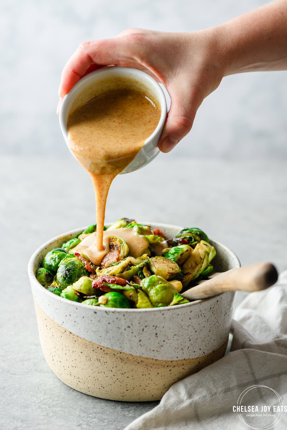 Hand pouring honey mustard sauce over a bowl of brussels sprouts with bacon