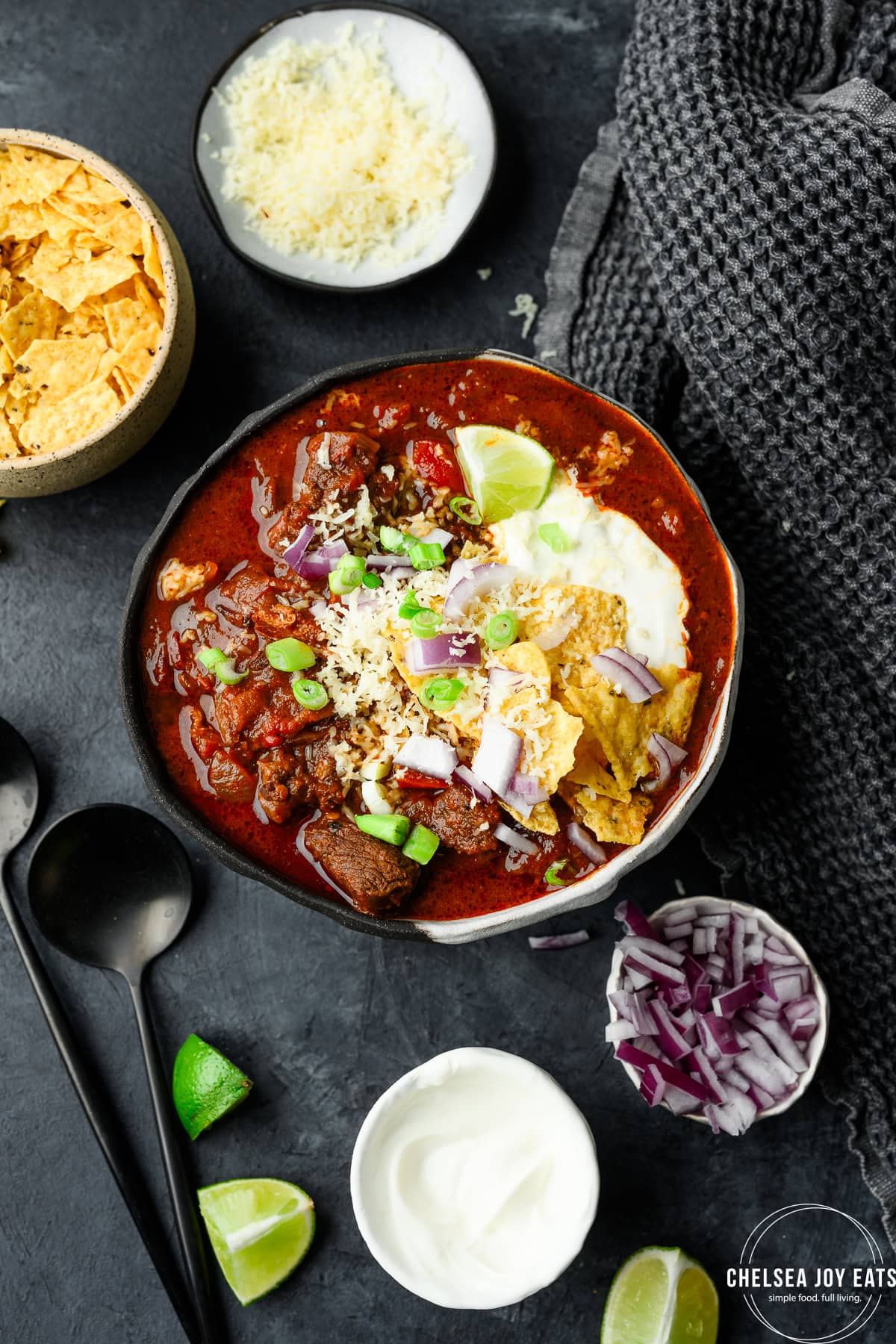Bowl of chuck roast chili topped with sour cream, crushed tortilla chips, cheese, and green onions