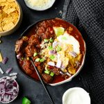 Bowl of chuck roast chili without beans topped with sour cream, crushed tortilla chips, and more toppings