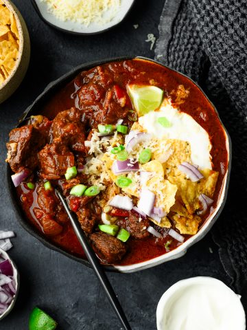 Bowl of chuck roast chili without beans topped with sour cream, crushed tortilla chips, and more toppings