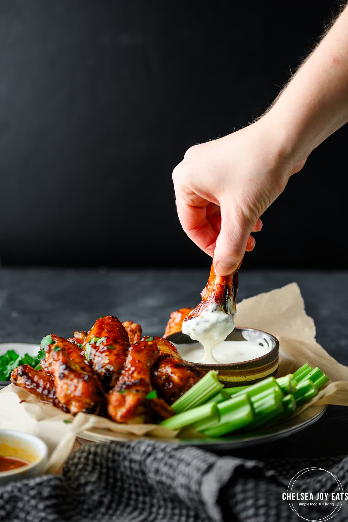 Hand dipping a hot honey chicken wing in blue cheese sauce