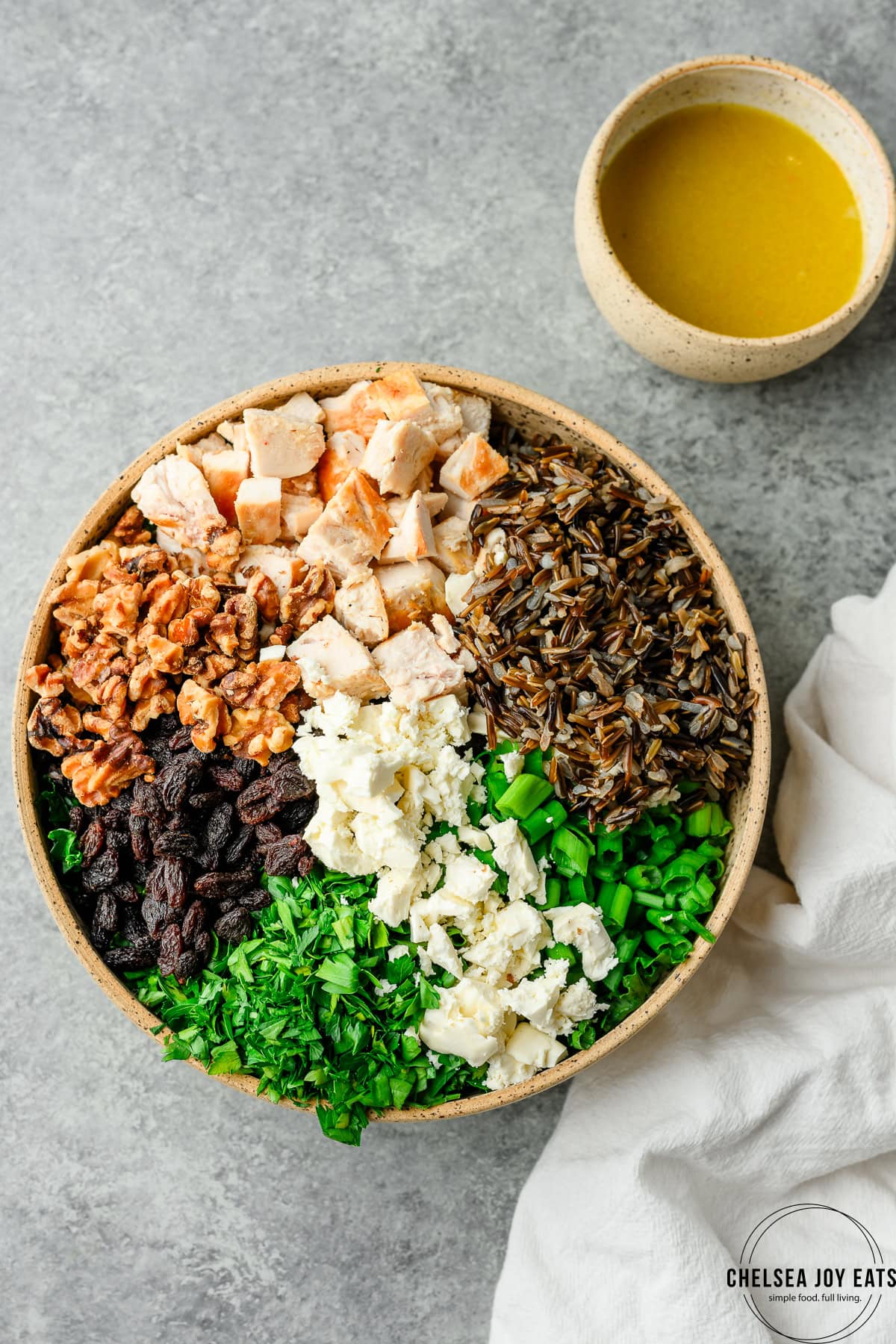 Bowl with salad ingredients, including wild rice, kale, chicken, feta cheese, walnuts, and raisins