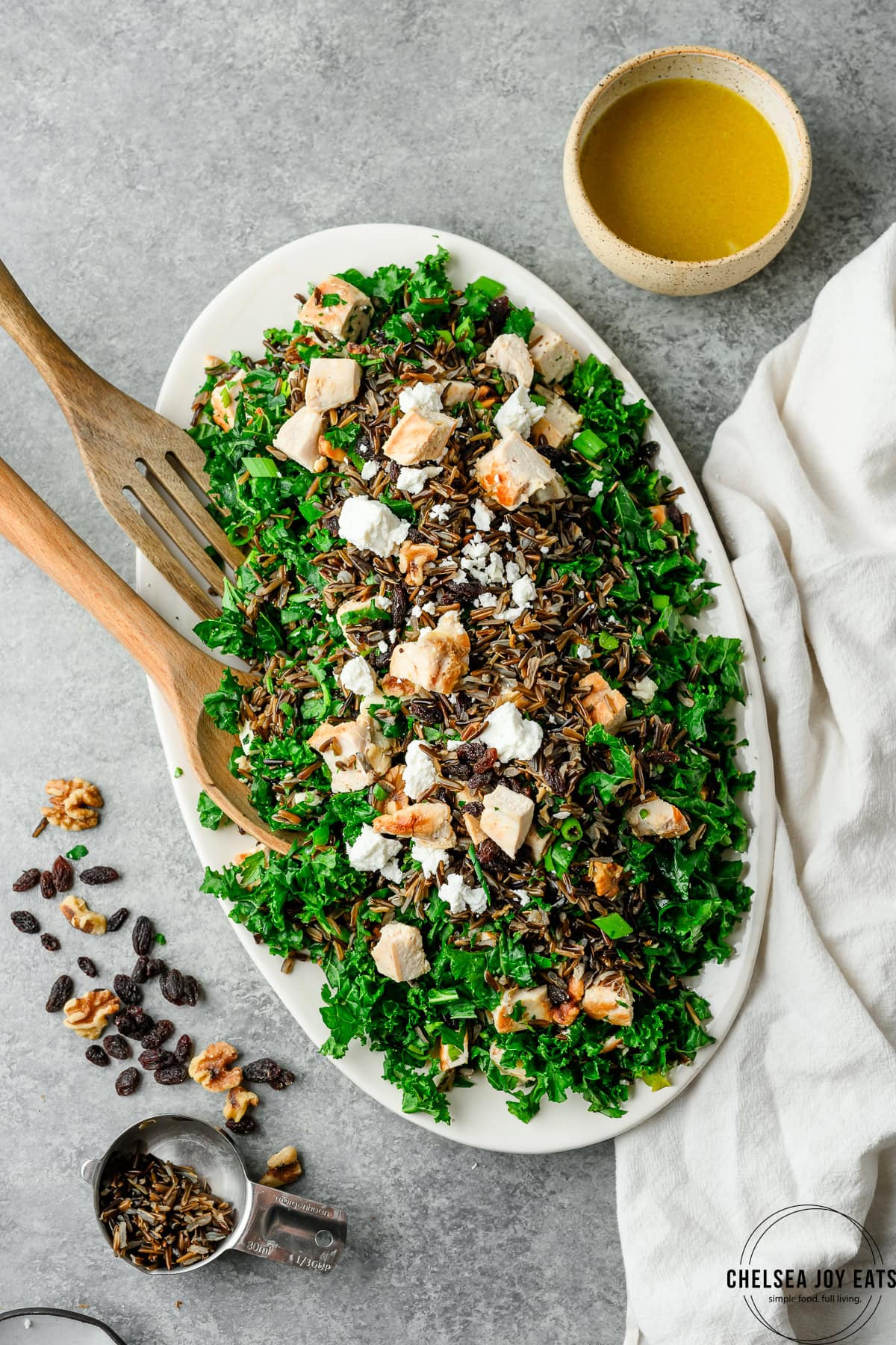 Overhead view of kale with wild rice, chicken raisins, and feta arranged on a platter, with orange dressing on the side