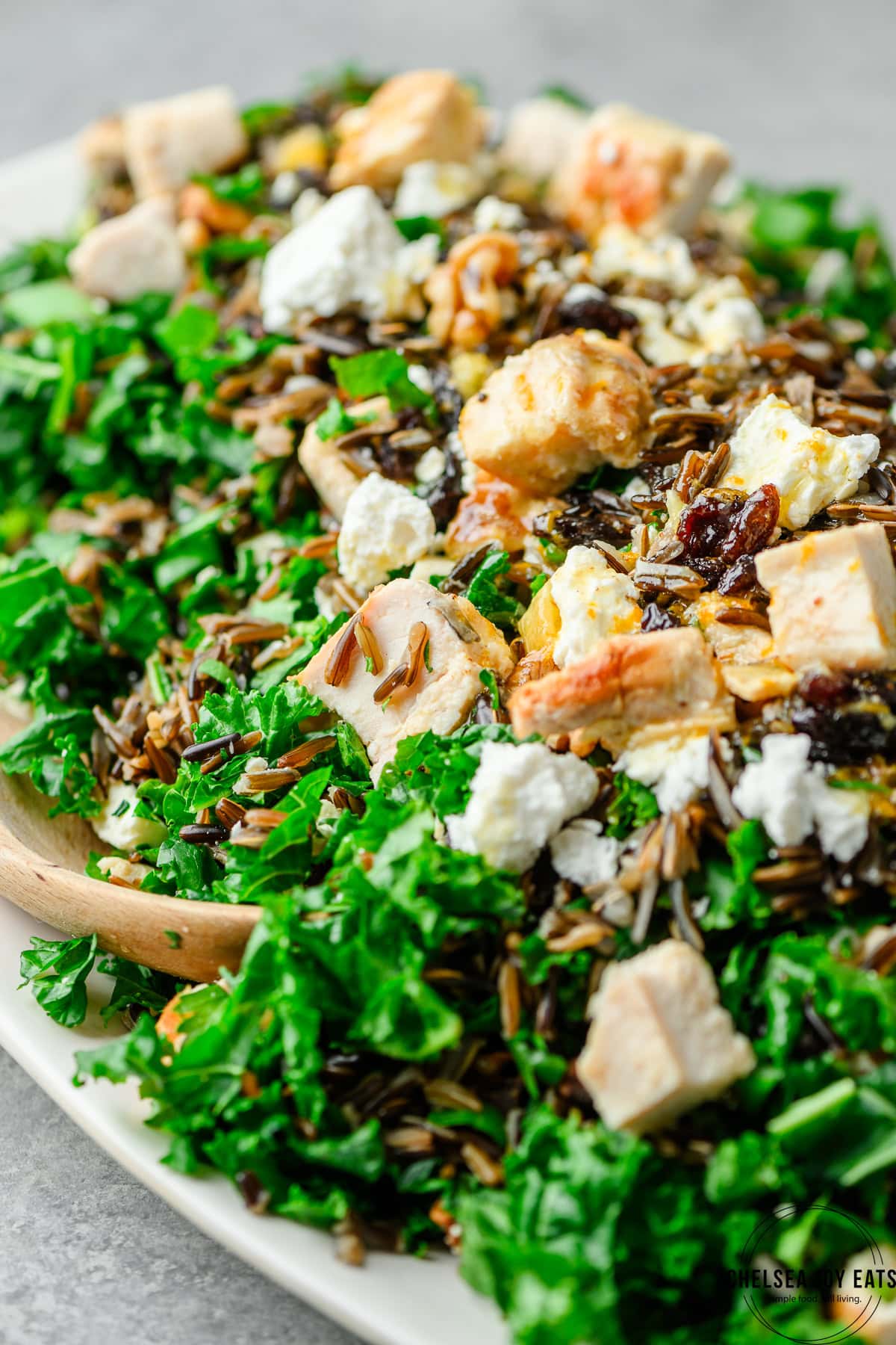 Closeup of chopped chicken, raisins, and feta atop a kale wild rice salad with orange dressing