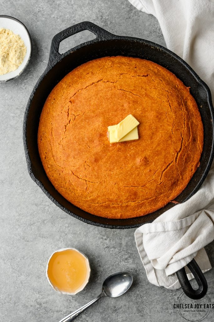 Overhead view of gluten free honey cornbread in a cast iron skillet with dabs of butter on top