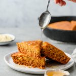 Gluten free cornbread stacked on a plate with a spoon drizzling honey overtop