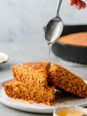 Gluten free cornbread stacked on a plate with a spoon drizzling honey overtop