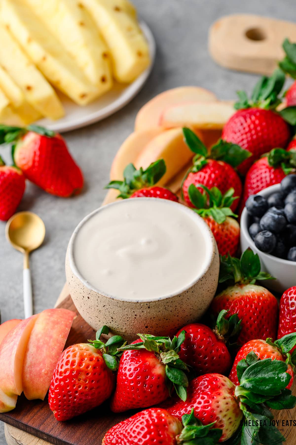 Bowl of cottage cheese fruit dip with fresh apples, strawberries, blueberries, and sliced pineapple alongside