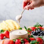 Dish with protein fruit dip surrounded by fresh strawberries, blueberries, and pineapple