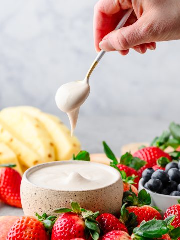 Dish with protein fruit dip surrounded by fresh strawberries, blueberries, and pineapple