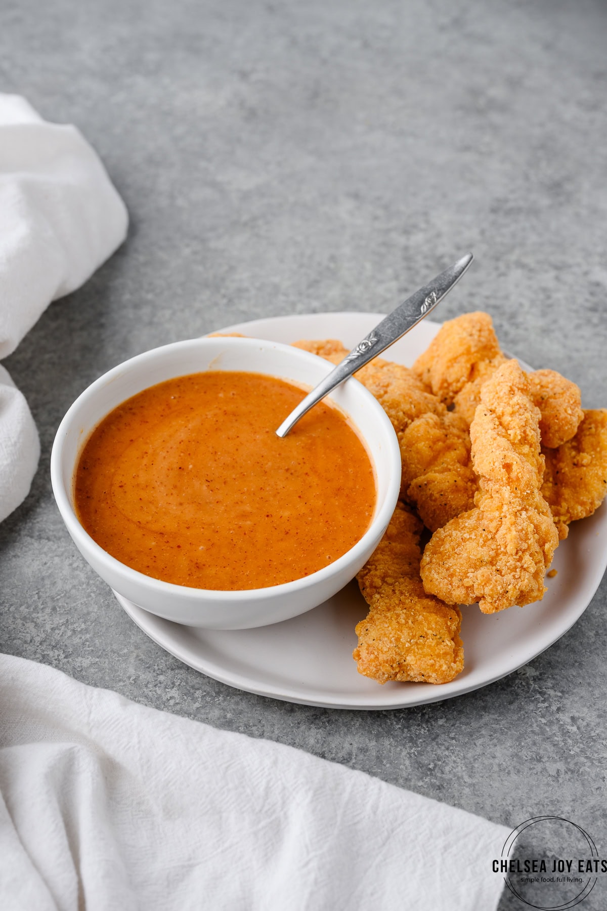 Bowl of hot honey mustard sauce on a plate with breaded chicken strips