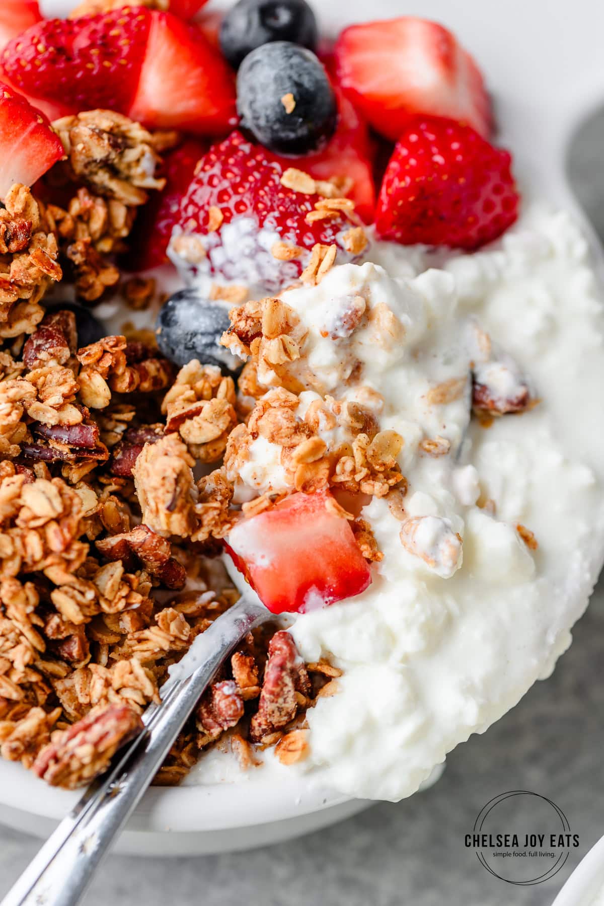 Closeup of a spoon digging in to a bowl of cottage cheese, granola, and fruit
