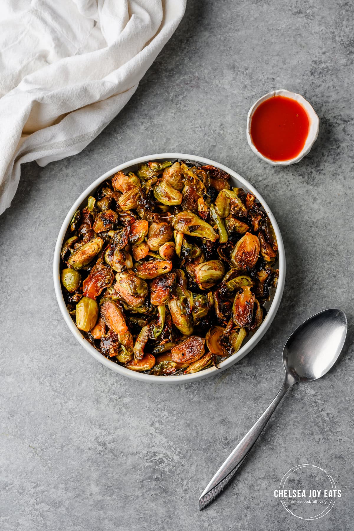 Serving bowl with hot honey glazed brussels sprouts and extra hot sauce alongside