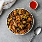 Serving bowl filled with saucy hot honey brussels sprouts with a serving spoon alongside