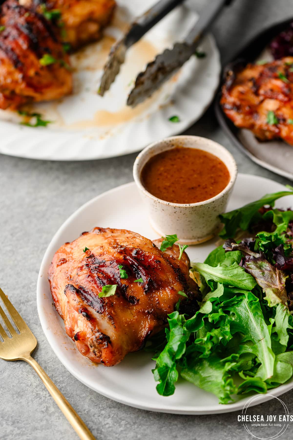 Plate with grilled chicken thigh and salad greens served with sauce alongside