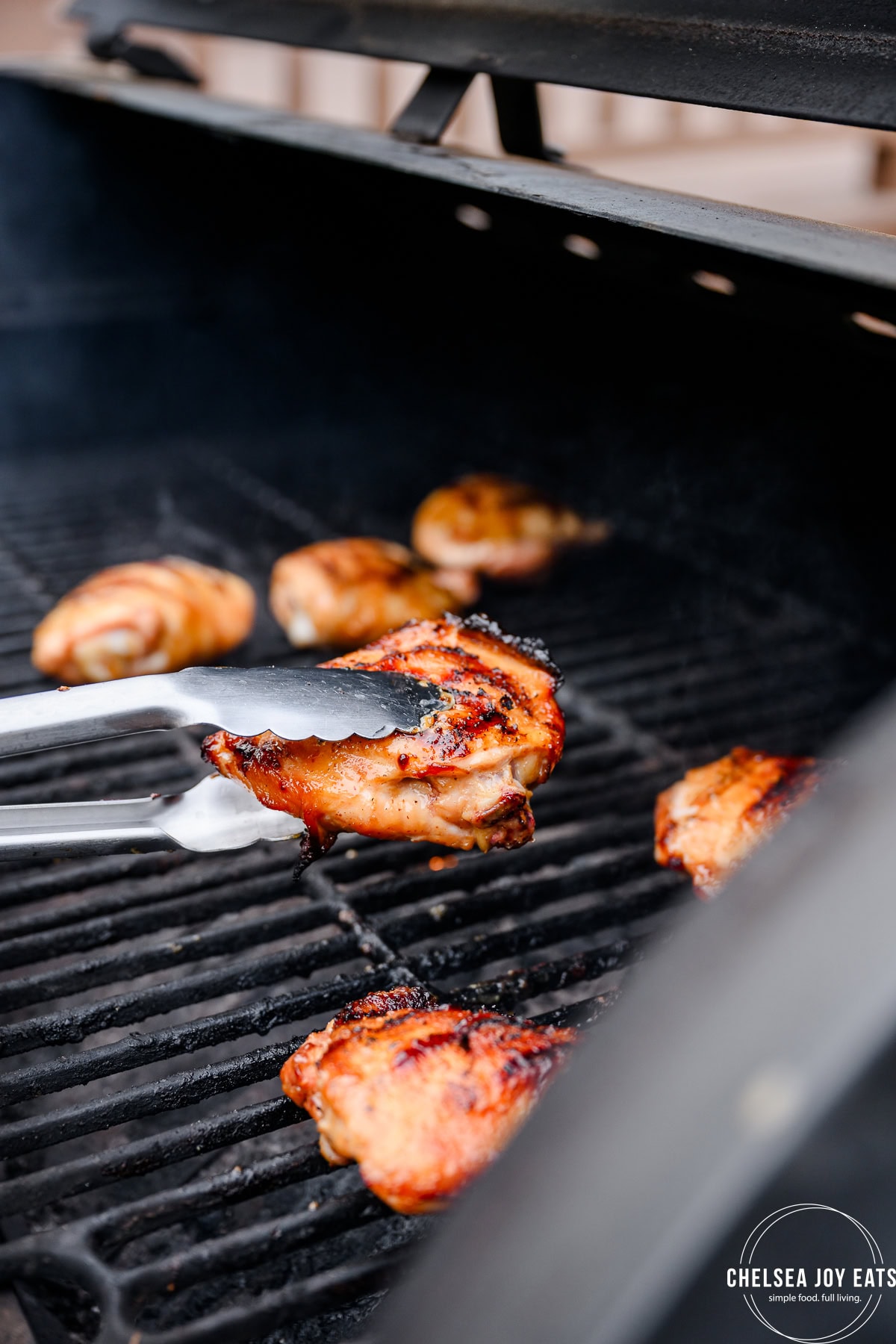 Kitchen tongs flipping grilled chicken thighs.