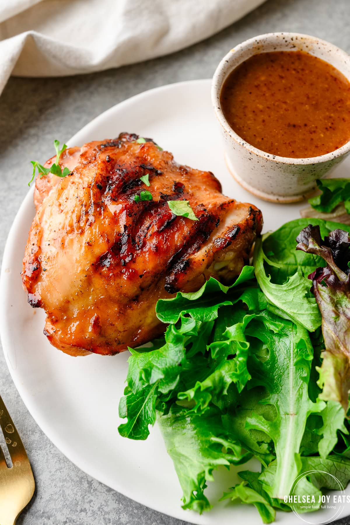 Closeup of a grilled Maple Dijon Chicken Thigh next to salad greens and extra sauce