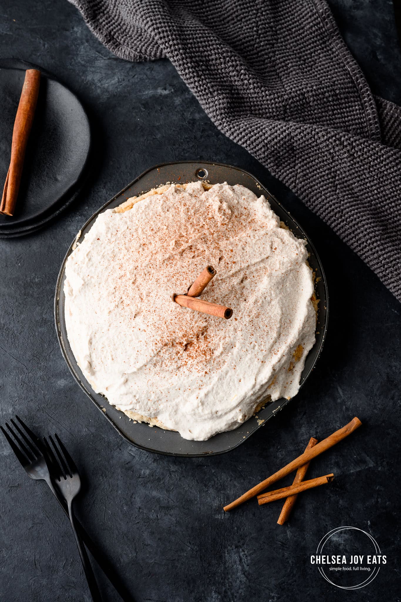 Overhead view of a no bake pumpkin pie topped with whipped cream, a dusting of cinnamon, and cinnamon sticks