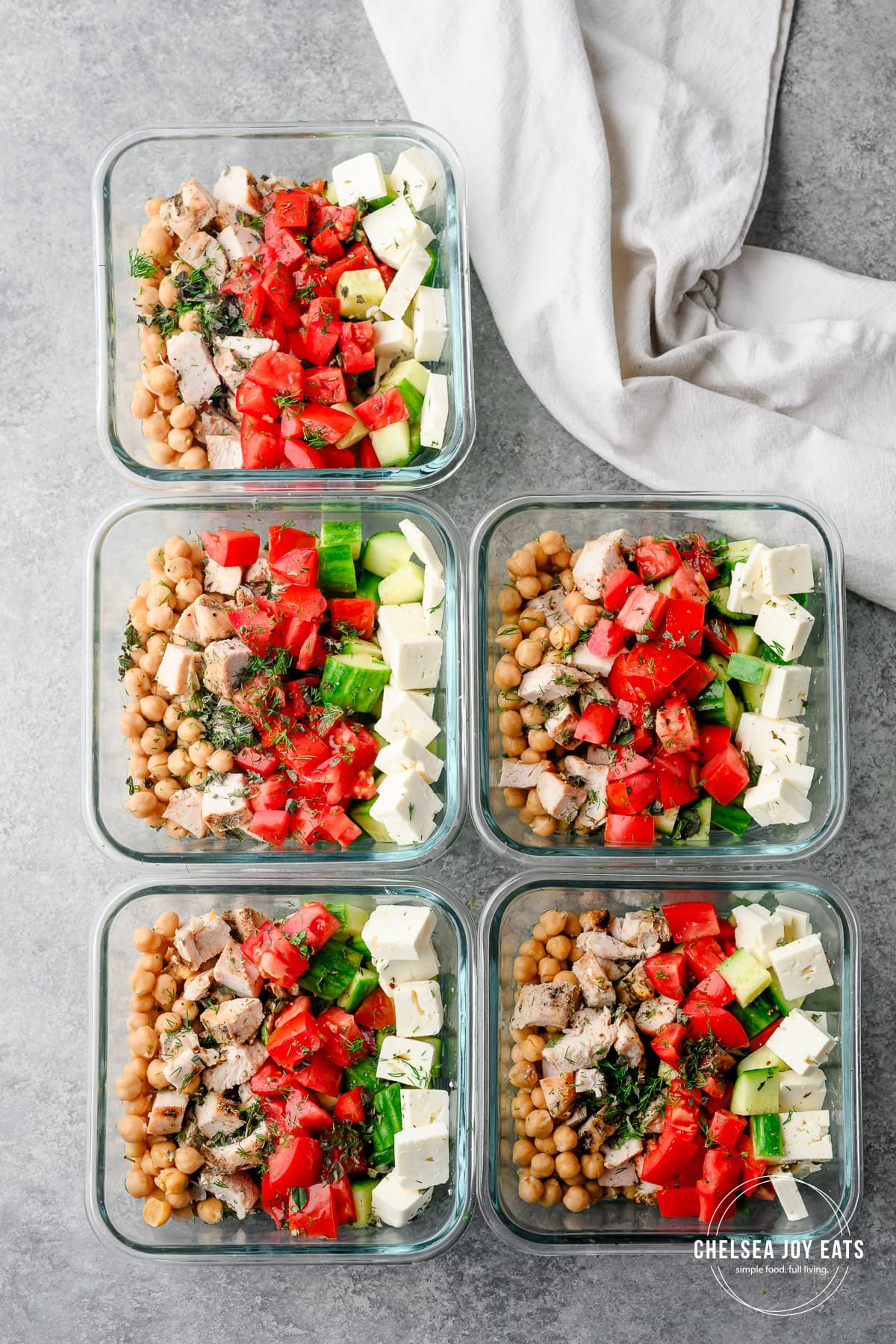 Five prepped Greek salad bowls with ingredients in neat rows