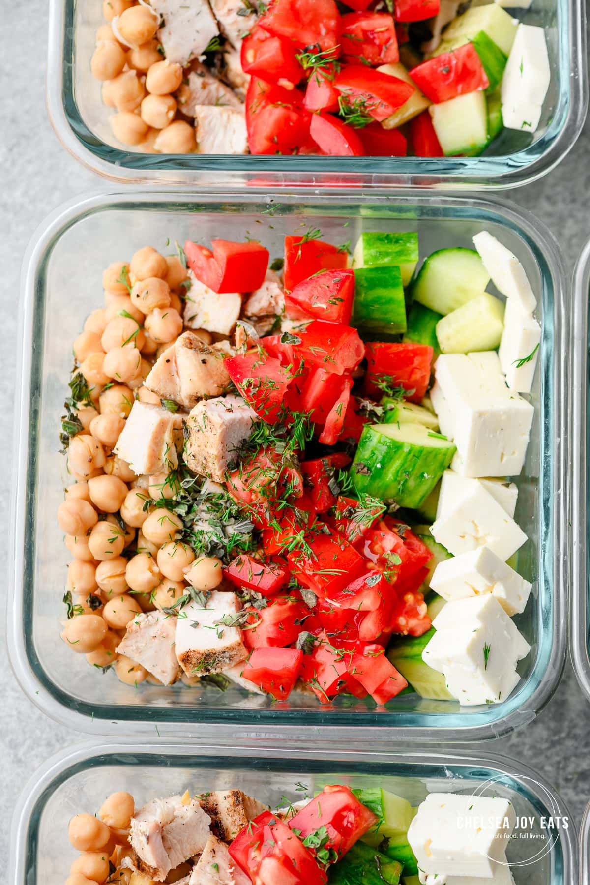 Closeup of Greek salad meal prep bowls with chickpeas, chicken, tomatoes, cucumber, and feta cheese