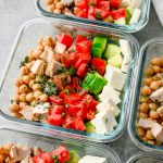 Square bowl with feta Greek salad topped with herbs and lemon vinaigrette