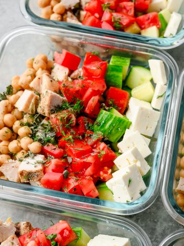 Square bowl with feta Greek salad topped with herbs and lemon vinaigrette