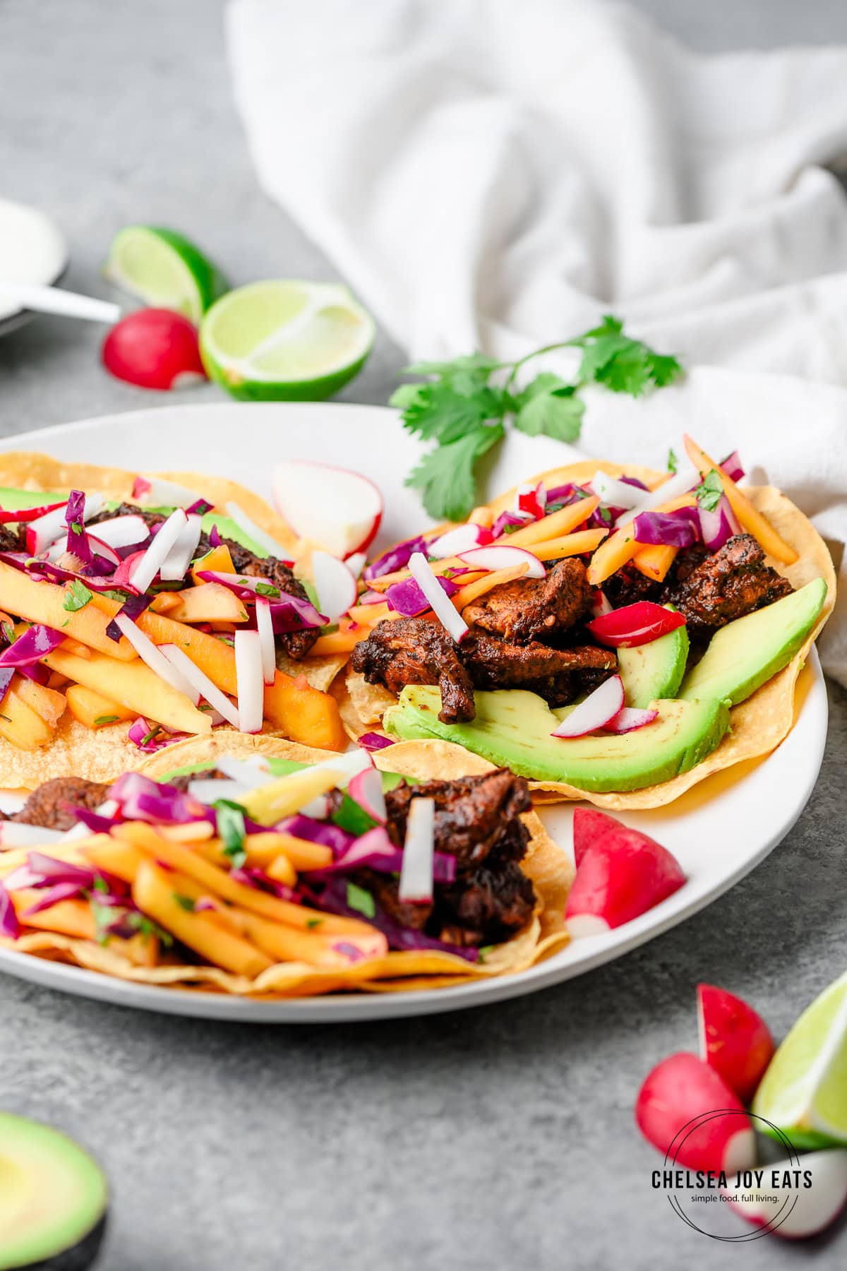 Closeup of ancho lime chicken tacos with avocado, mango slaw, and radish
