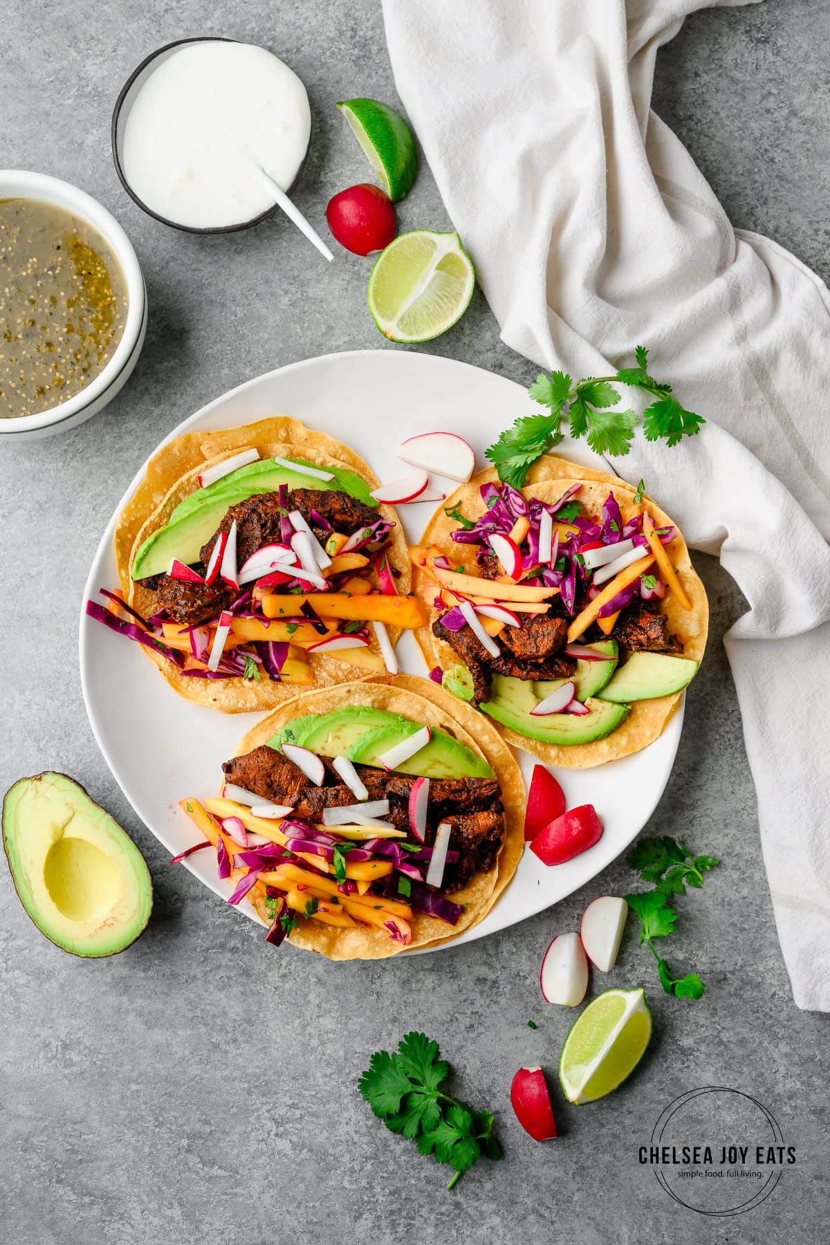 Bird's eye view of ancho chicken tacos assembled on a plate with mango slaw and avocado