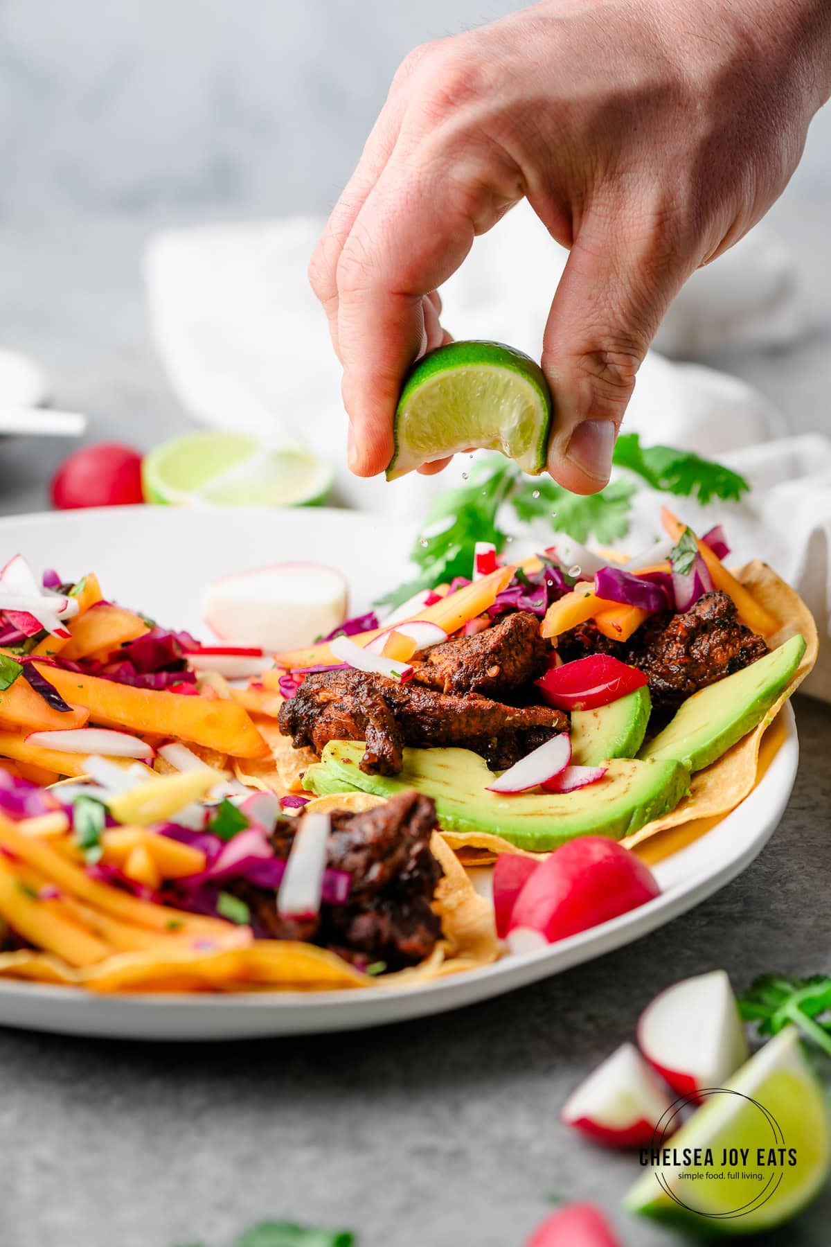 Person squeezing fresh lime juice over ancho chicken tacos with mango slaw